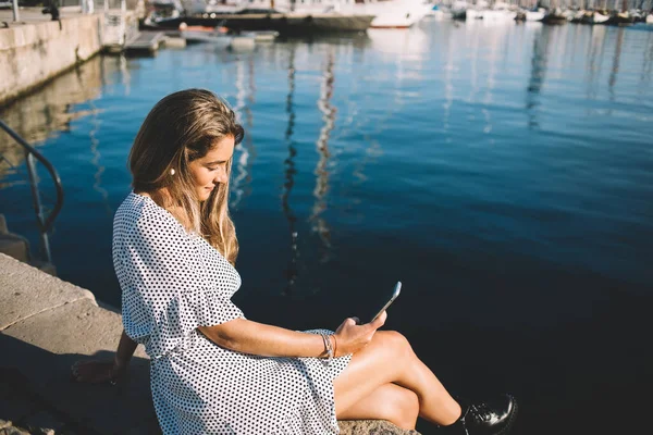 地中海の近くの港で休息を取る魅力的な女性観光客や旅行者のための情報やアドバイスを検索するためのスマートフォンのガジェットを使用して 白人ヒップスター女の子読書が受け取ったSms — ストック写真