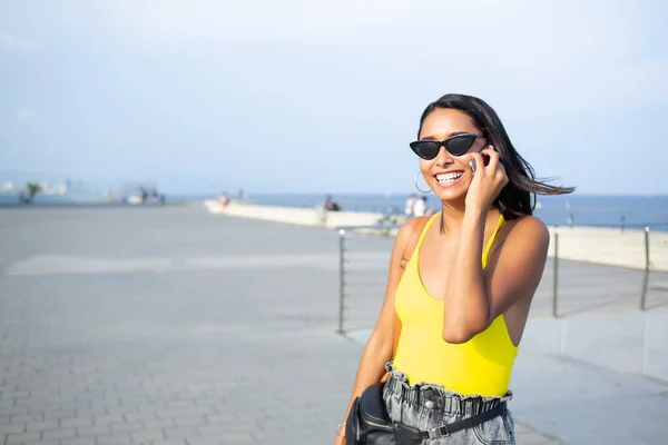 Half length portrait of cheerful female tourist in black sunglasses phoning via cell app for communicate during travel vacations, toothy carefree hipster girl enjoying friendly smartphone talking