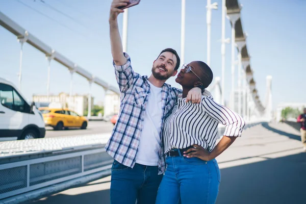 アフリカ系アメリカ人女性を受け入れている携帯電話を使用して自慰行為をするカジュアルな服の中で楽しい髭の男を笑顔通りを散歩 — ストック写真
