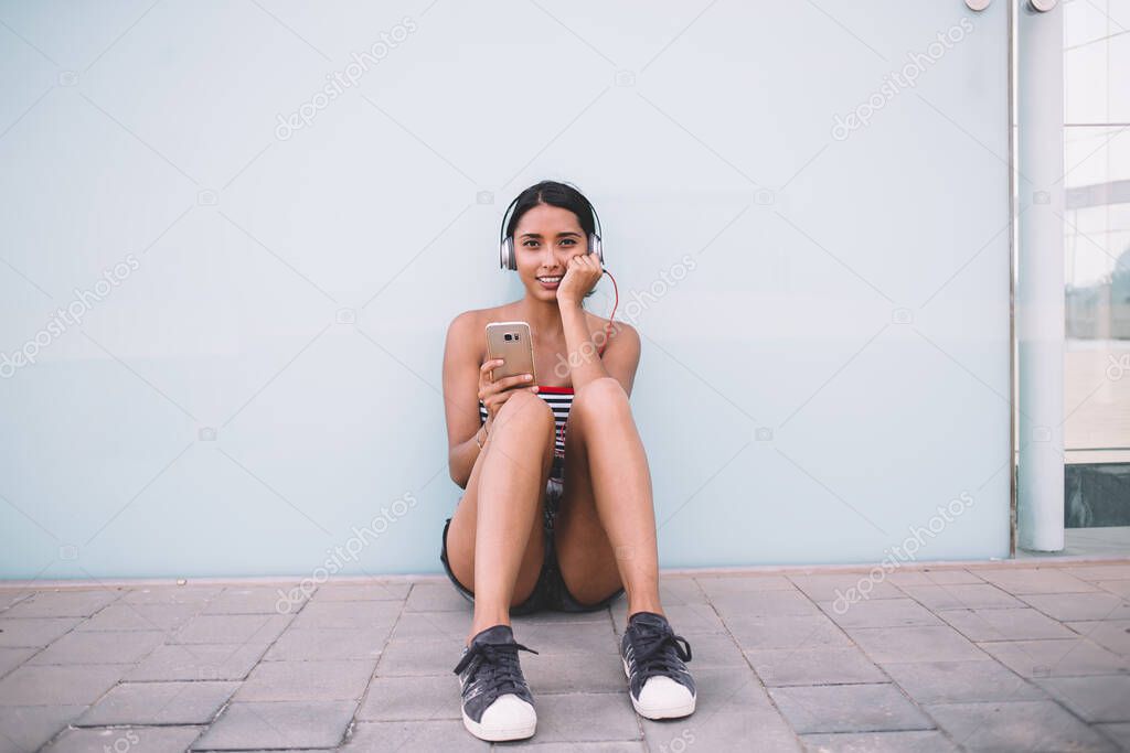 Portrait of pretty cute hipster girl spending leisure in city enjoying sound playlist with popular track connected to 4g wireless on smartphone gadget for listening electronic audio records