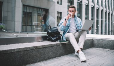 Akıllı saatli ve kulaklıklı genç adamlar sıradan kıyafetler giyip kahve içerken şehirdeki cam bir bankta dizlerinin üstüne çöküp dizlerinin üstüne çöküp gözlerini kaçırıyorlar.