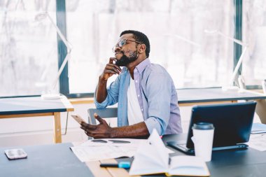 Gülümseyen, rahat giyimli, cep telefonu tutan, dizüstü bilgisayarlı ve defterli Afro-Amerikan erkeği.  
