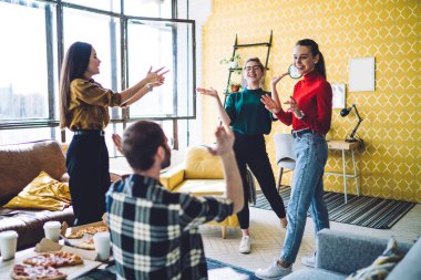Neşeli insanlar gündelik kıyafetleriyle konuşuyorlar ve el kol hareketleri yapıyorlar. Bir yandan da pizza kutuları ve yemek kupalarıyla modern apartmanda oturuyorlar.