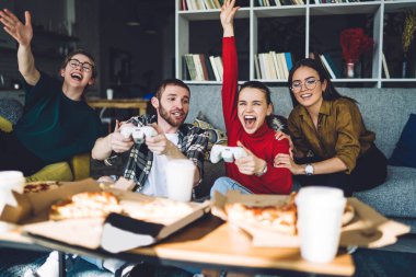 Rahat rahat video oyunu oynayan, rahat koltukta takılan ve modern çatı katında pizza keyfi yapan günümüzün rahat arkadaşları.