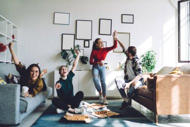 Mutlu iyimser gençler TV 'de maç izlerken başarıyı kutlarken beşlik çakıyor ve pizza yerken kollarını kaldırıyor.