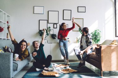 Mutlu çığlıklar atan neşeli grup pizza yiyor ve televizyonda futbol takımının zaferini kutluyor beşlik bir hareketle ve oturma odasında kollarını kaldırarak.