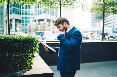 Mavili takım elbiseli yöneticinin ara verildiğinde caddede ofis binasının yanında dururken tablette büyük ilgi uyandıran haberlerle yan görünümü