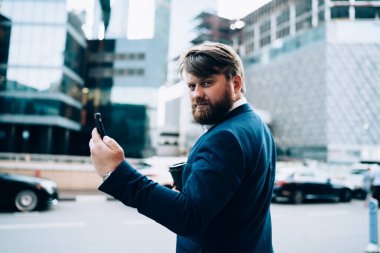 Ciddi bir adamın elinde telefonla arka planda şehir trafiğinin arka planındaki kameraya bakması.