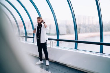 Beyaz tişörtlü, spor ayakkabılı, kulaklık takan, yaya köprüsünde camla dikilen müzik dinleyen havalı bir adam.