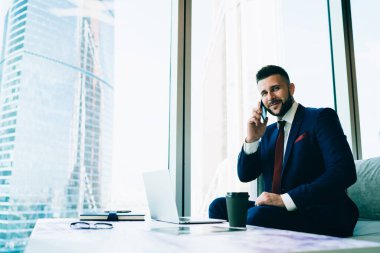 Resmi olarak başarılı bir yönetici gülümseyen ve kameraya bakarken masanın yanında dizüstü bilgisayarla oturup içki ısmarlar ve ofisteki akıllı telefondan konuşur.
