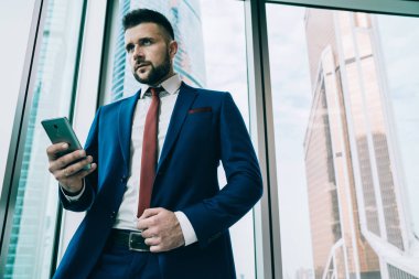 Stratejik plan geliştirirken ve gökdelenin çağdaş ofisinde akıllı telefon ile etkileşime girerken ciddi bir yetişkin kararlı patron çözme sorunundan