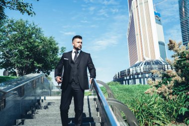 Başarılı, takım elbiseli iş adamı merdivenlerden inip tırabzanlara yaslanıyor ve gündüzleri iş merkezindeki caddeye bakıyor.