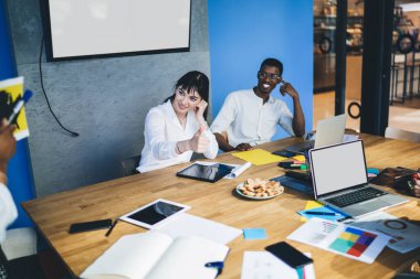 Modern çok ırklı çalışanlar istatistik kağıtları ve dizüstü bilgisayarla toplantı masasında monitör ekranına karşı bir araya gelerek şirket stratejisi hakkında konuşuyorlar. 