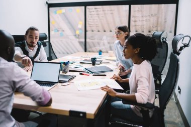 Milenyum döneminden kalma çok ırklı meslektaşlar öğleden sonra iyi aydınlatılmış çağdaş brifing ofisinde iş konuları üzerinde yoğunlaşıp giyindiler.