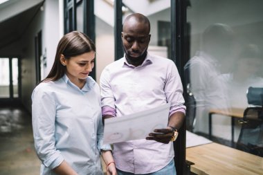 İş yerinde gülümseyen genç bir bayanın çizelgesini göstermesiyle başlayan, günlük kıyafetleriyle başarılı Afrikalı erkek.