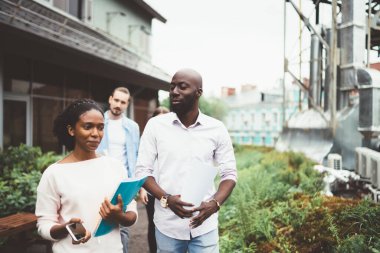 Şehir ve fabrika borularının arka planına karşı bina yakınlarında yürürken insanlar işi tartışıyor ve belgeleri ellerinde tutuyorlar.
