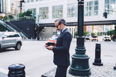 Gözlüklü ve siyah kostümlü yakışıklı, beyaz saçlı işadamının New York 'ta arka grubunda akıllı telefonlara tıklaması.