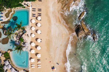 Açık havuzu ve güneş pansiyonları olan ilk hat plaj otelinin havadan görünüşü. Yaz tatillerinin kuş bakışı manzarası, turkuaz deniz suyu ve temiz kum kıyısındaki şemsiyeler.