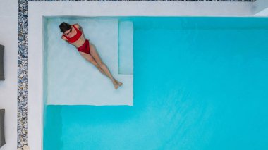 Havadan görünüşlü, kırmızı mayo giyen kaygısız kadın turist yaz tatilinde lüks modern villa havuzunda dinleniyor. Modaya uygun bir kadın kiralık evde dinleniyor.