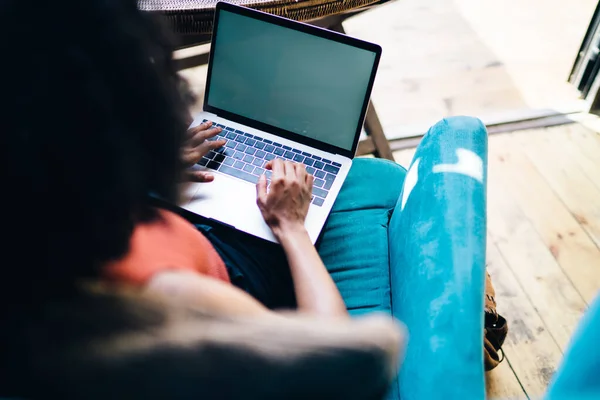 坐在户外露台咖啡厅蓝色沙发上 穿着休闲装 在笔记本电脑上冲浪的卷曲头发的少数民族女性如图所示 — 图库照片