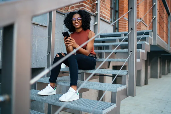 Afro Americano Feliz Encaracolado Fêmea Casual Desgaste Óculos Usando Smartphone — Fotografia de Stock