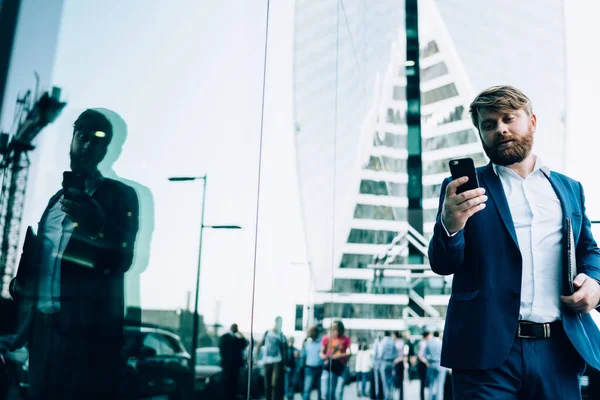 身着雅致的蓝色西装和白衬衫 头戴智能电话屏幕 站在大街上 面对着闹市区模糊的现代高楼和镜面的成年男子 — 图库照片