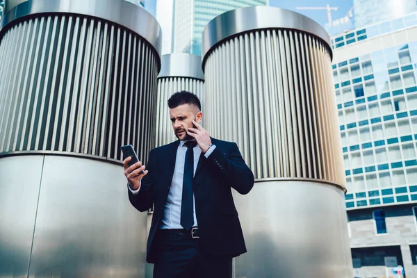 Zmatený Vousatý Chlap Obleku Mračení Prohlížení Zpráv Smartphonu Zatímco Stojí — Stock fotografie