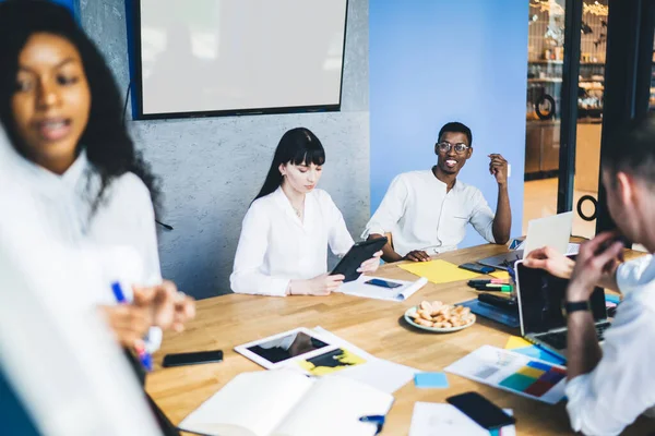 ホワイトフォーマルな服装の多人種の同僚のグループは 会社での作業計画について会話をしながら ホワイトモニター画面に対する文書やラップトップと会議テーブルに座っています — ストック写真