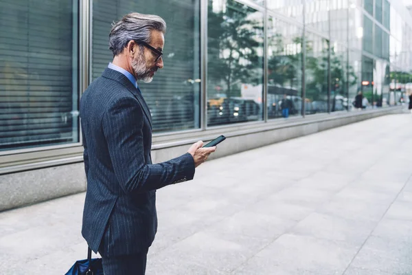 ニューヨークの空の街の通りに電話番号を入力スタイリッシュな暗いビジネススーツで灰色のひげを持つ成功した男の側面図 — ストック写真