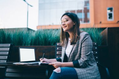 Vizyon koruması için göz takan zeki kadın yazar serbest çalışıyor güneşli bir günde dışarıda eğleniyor, bin yıllık kadın blogcu laptopu kullanarak ekran modelini yapmayı düşünüyor.