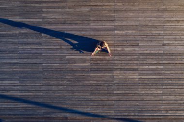 Spor kıyafetli sıska bir kadın Lotus pozisyonunda oturuyor ve tahtadan zeminde meditasyon yapıyor.