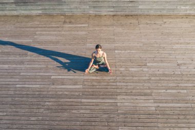 Dinginlik ve ahenkle dolu genç bir kadının manzarası. Nilüfer pozisyonunda oturmuş, ahşap zeminde dinleniyor.