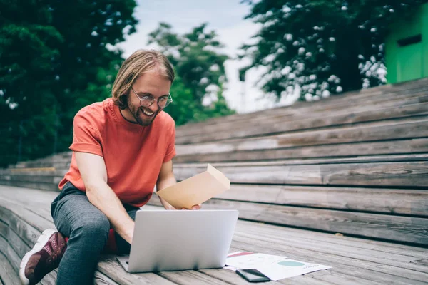 Junger Trendiger Hipster Mit Brille Surft Laptop Während Zeitungsberichte Hält — Stockfoto