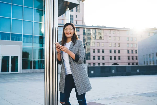 Счастливая Женщина Повседневном Наряде Очках Улыбается Думает Пользуясь Смартфоном Столба — стоковое фото