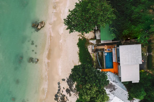 Aerial top view of beachfront villa surrounded be green trees. Bird\'s eye tropical view of summer holidays background, turquoise water seashore with clean sand coastline. Paradise rest