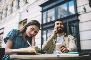 Genç bir kadın not defterine yazıp saçlarını düzeltirken sokak restoranında erkek arkadaşının yanında oturmuş akıllı telefondan konuşuyordu.