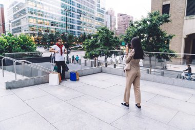 Uzun saçlı, stil sahibi bir kadının, modern şehrin arka planında cam çitin önünde duran, alışveriş torbalarıyla neşeli bir adamın fotoğrafını çekişi.