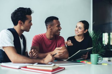 Çok ırklı, zeki, güler yüzlü iş arkadaşları gündelik giysiler içinde masada oturmuş kağıt belgelerle akıllı telefonları modern ışık yaratıcı çalışma alanına koyuyorlar. 