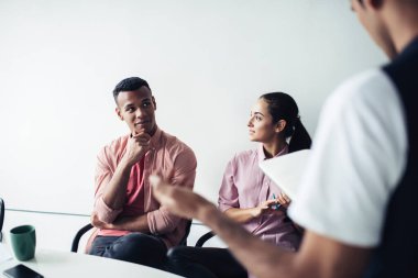 Çok ırklı, entellektüel, gündelik giysiler içindeki iş arkadaşları akıllı telefonlar ve bir fincan kahveyle modern, aydınlık ofis çalışma alanında oturuyorlar. 