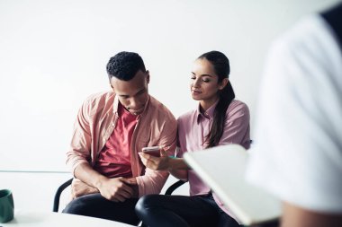 Akıllı telefon cihazlı çekici yeniyetme kız sosyal ağlarda el yazısı okuyor ve yanında oturan erkek meslektaşına yayınını gösteriyor. Çeşitli erkek ve kadınlar, kablosuz 4G ile akıllı telefon kullanıyorlar.