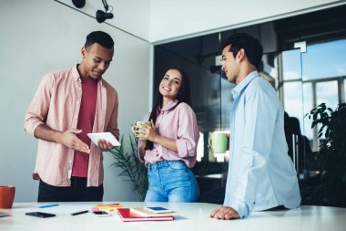 Çok kültürlü, güler yüzlü entellektüel iş arkadaşları dolapların karşısındaki masada kahve fincanlarını tutuyorlar.