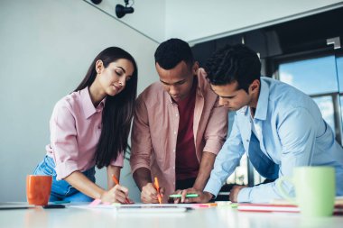 İş günü kapalı alanda iş birliği yapan zeki meslektaşlar, genç erkek ve kadın çalışanlar strateji analizi yaparak beyin fırtınası ve takım çalışmasının keyfini çıkarıyorlar.