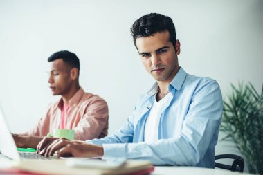 İspanyol erkek metin yazarlarının portresi modern dizüstü bilgisayarda uygulama için makale hazırlamak için zaman harcıyor, veritabanı bilgileriyle online çalışan çok kültürlü programcılar