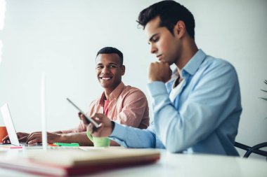 Amerikalı neşeli yöneticinin portresi kameraya gülümserken İspanyol meslektaşı cep telefonu cihazıyla iş ortaklarıyla iletişim kuruyor ve mesajlaşıyor.