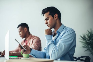Milenyum İspanyol programcı, modern çalışma alanındaki masa başında çalışırken akıllı telefon uyarısını kontrol ediyor, genç erkek, mobil internet sitesinde pazar haberleri okuyor, 4G 'ye bağlı.