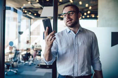 Optik gözlüklü beyaz erkek komisyoncu ofis internetine bağlı finansal akıllı telefon web sitesinde analitik para alışverişini kontrol ediyor, resmi giyinmiş girişimci cep telefonu e-postası alıyor