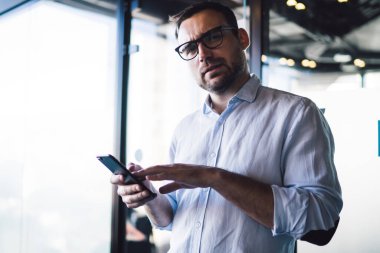 Optik gözlüklü şaşkın erkek girişimcinin yarım boy portresi cep telefonu sorununu çözmek için kameraya bakarken göz koruması sağlar.