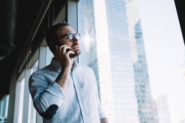 Klasik gözlük takan Kafkas işvereni iş günü hizmet danışmanlığı için cep telefonu aygıtı kullanıyor, genç işadamı cep telefonu uygulaması ile ortağına sesleniyor.