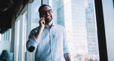 Şirket ortağıyla yapılan akıllı telefon iletişimi sırasında kameraya gülümseyen klasik göz giysili neşeli erkek bankacının yarım boy portresi, mutlu iş adamı çevrimiçi konuşma için mobil cihaz kullanıyor.