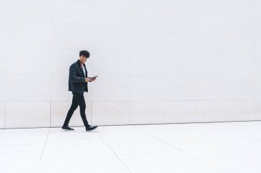 Modern stil, güler yüzlü, kendinden emin, Afro-Amerikan bir adamın gün ışığında şehir caddesinde yürürken tablet üzerinde gezinmesinin yan görüntüsü.